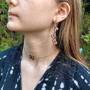 May include: A gold-colored chain necklace and earrings set. The necklace features a single butterfly pendant, while the earrings have a cascading design of three butterflies. The butterflies have orange and black details.