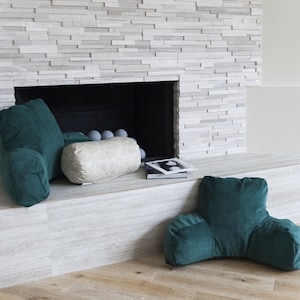 Puede incluir: Una escena de sala de estar acogedora con tres cojines. Dos son cojines de respaldo de color verde azulado, y uno es un coj&iacute;n cil&iacute;ndrico crema con un patr&oacute;n geom&eacute;trico. Los cojines est&aacute;n colocados cerca de una chimenea.