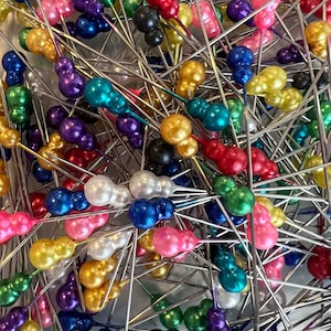 May include: A large assortment of colorful glass-headed pins with silver metal shafts. The heads are in various colors, including red, pink, blue, green, purple, gold, and white.
