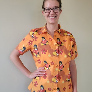 Può includere: Una camicia a maniche corte con bottoni di colore arancione con un motivo di pinguini che indossano collane di fiori rosse e bianche.