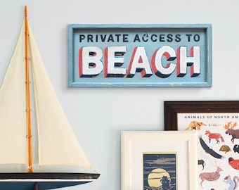 May include: A white wooden shelf with a model sailboat, a framed print of animals of North America, a framed print of a moonlit scene, and a wooden sign that reads "Private Access to Beach".
