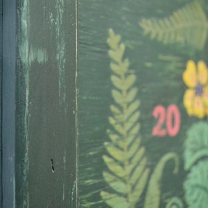 May include: A green wooden sign with a painted floral design. The sign has the number 20 painted in pink on it.