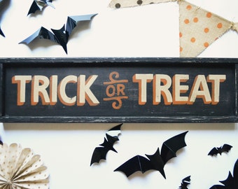 May include: A black wooden sign with white and orange lettering that reads "Trick or Treat". The sign is surrounded by black bats and brown and white polka dot bunting.