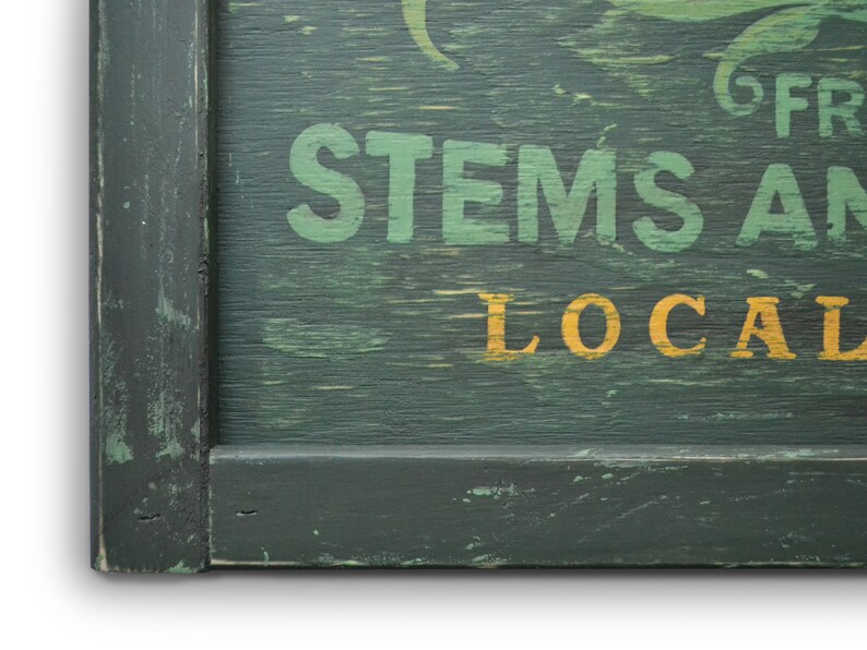 May include: A green wooden sign with white painted text that reads "STEMS AND LOCAL" in a vintage style font. The sign has a dark green frame.