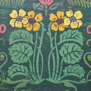 May include: A green wooden sign with yellow flowers and green leaves painted on it. The numbers 20 and 05 are painted in pink on either side of the flowers.