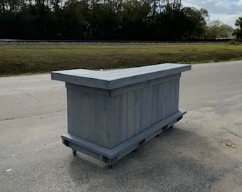 May include: A gray wooden bar with a countertop and a lower shelf. The bar is on wheels and has a corner design.