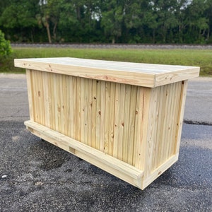 May include: A wooden bar counter with a natural wood finish. The counter is made of vertical planks and has a flat top.