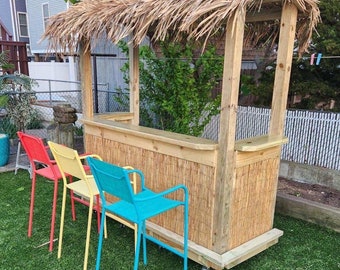 May include: A wooden tiki bar with a thatched roof, featuring a wooden countertop and a bamboo-style front panel. Three colorful chairs are positioned in front of the bar, with a red chair, a yellow chair, and a blue chair.