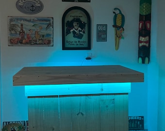May include: A wooden bar cart with a light blue LED strip underneath the top shelf. The cart has a rustic look and is on wheels. The cart is decorated with nautical themed signs, including "Feeling Nauti", "It's 5 O'Clock Somewhere", "Dead Men Tell No Tales", "Tavern", and "Old Enough To Care".