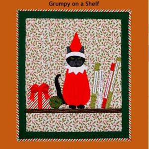Könnte beinhalten: Ein Stoffkunstwerk mit einer schwarzen Katze als Elf, mit rotem Outfit und Hut, auf einem Regal. Der Hintergrund hat ein Stechpalmenmuster. Der Text "Trouble & Boo Designs" und "Grumpy on a Shelf" befindet sich oben.