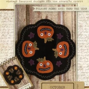 May include: A black felt mat featuring four orange pumpkin faces with stitched details and purple stars. The text reads Buttermilk Basin, Folkart Penny Mats Thru The Year, October, and Diameter - 8.5 inches. The design includes a scalloped edge.
