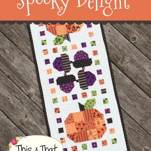 Può includere: Un runner trapuntato rettangolare intitolato Spooky Delight di This & That. Il design presenta zucche arancioni e ghiande viola su sfondo bianco, incorniciato da un bordo marrone scuro con piccoli punti arancioni e piccoli quadrati.