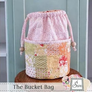 May include: A patchwork bucket bag with a drawstring closure. The bag features a variety of floral and geometric patterns in shades of yellow, orange, and green. The top portion is a light pink fabric with printed text. Wooden beads accent the drawstring.