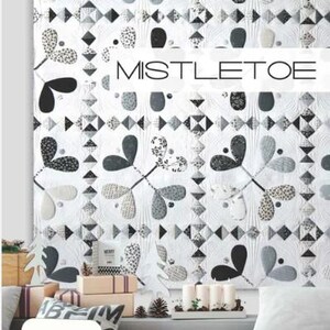 Puede incluir: Un edredón blanco con un patrón repetido de hojas de muérdago estilizadas en negro, gris y blanco. La palabra "MISTLETOE" se muestra en el edredón. El edredón forma parte de una colección temática navideña.