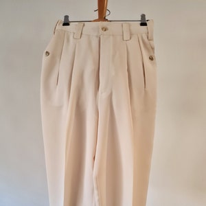 Könnte beinhalten: Eine cremefarbene Hose mit Falten, Knopfleiste und Seitentaschen.
