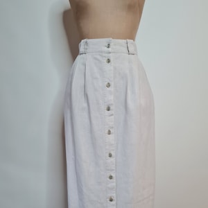 Può includere: Una lunga gonna di lino bianca con chiusura a bottoni sul davanti e vita alta. La gonna ha una texture sottile ed è uno stile classico e senza tempo.