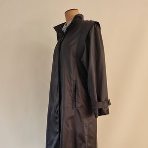 May include: A long black raincoat with a collar and a single pocket on the left side. The raincoat has a belt and a button closure.