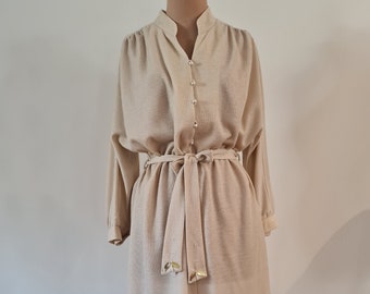 May include: A long-sleeved, beige dress with a button-up front and a self-tie belt. The dress has a slightly puffed sleeve and a relaxed fit.