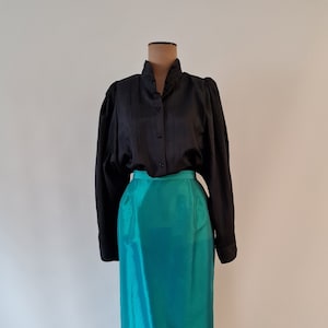 Puede incluir: Una falda de satén turquesa con una blusa negra de botones en un maniquí.