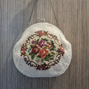 May include: A white beaded purse with a floral embroidery design. The purse has a round shape and a silver chain strap.