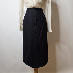 May include: A cream-coloured button-down shirt with two front pockets is paired with a black button-front skirt. The skirt is knee-length and has a tailored fit. The outfit is displayed on a mannequin.