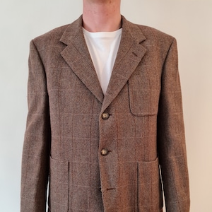 May include: A brown tweed blazer with a herringbone pattern and two flap pockets. The blazer has a three-button closure.