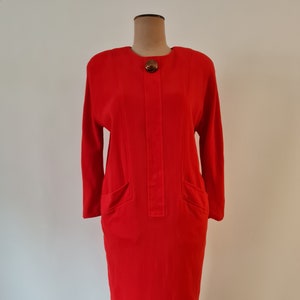 Könnte beinhalten: Ein rotes Kleid mit langen Ärmeln und einem einzigen Knopfverschluss am Ausschnitt. Das Kleid hat zwei Taschen vorne und eine figurbetonte Silhouette.