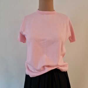 May include: A pink short-sleeved sweater on a mannequin. The sweater is made of a soft, knitted fabric and has a crew neckline.
