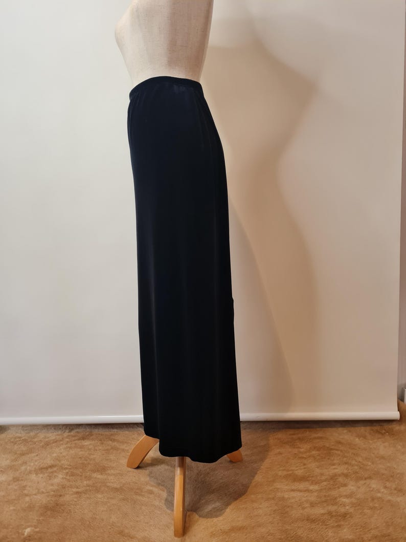 May include: A black maxi skirt made of a soft, stretchy fabric. The skirt is fitted at the waist and flows out to the hem.