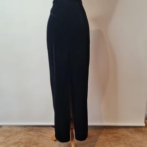 May include: A black velvet maxi skirt with a center slit. The skirt is on a wooden mannequin.