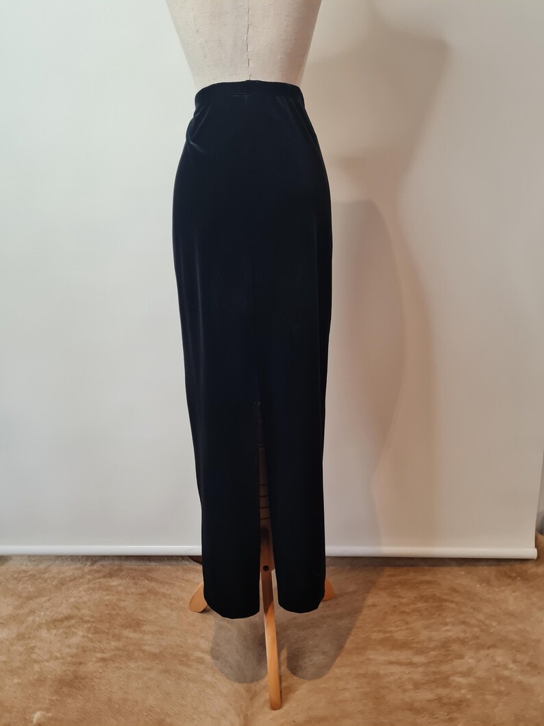 May include: A black velvet maxi skirt with a center slit. The skirt is on a wooden mannequin.