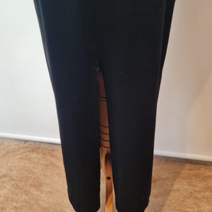 May include: Black velvet maxi dress with a high slit in the back. The dress is on a wooden hanger.