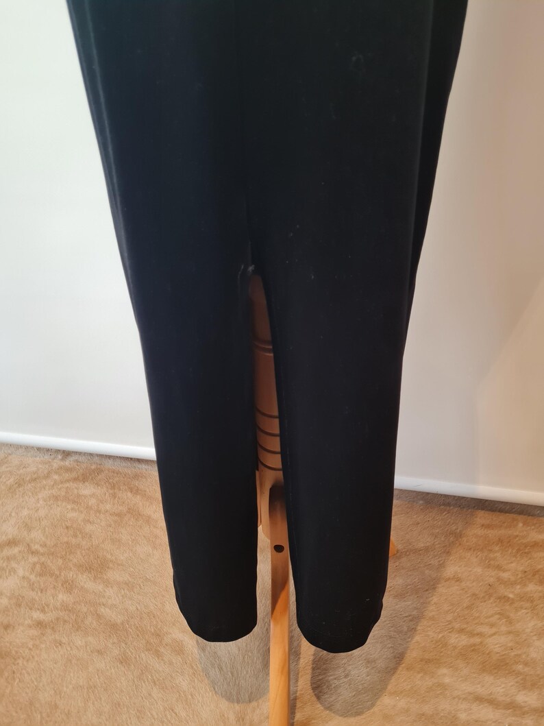 May include: Black velvet maxi dress with a high slit in the back. The dress is on a wooden hanger.