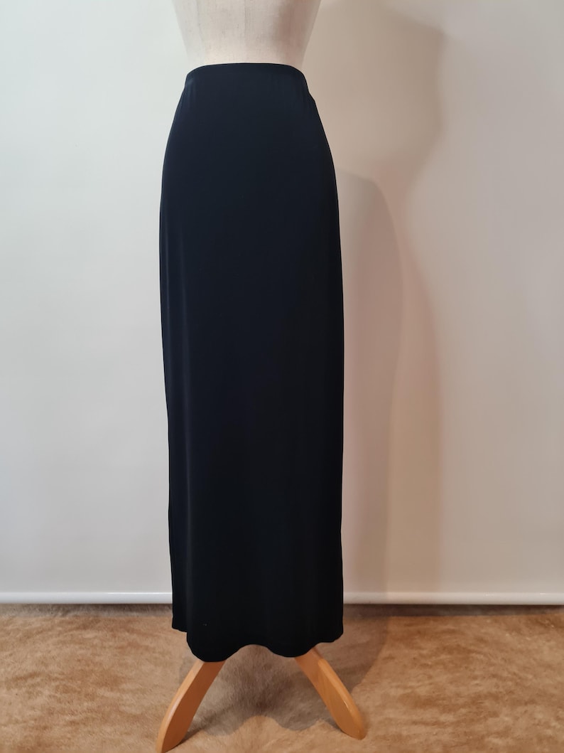 May include: A long black skirt made of a smooth fabric. The skirt is on a mannequin and is displayed against a white background.