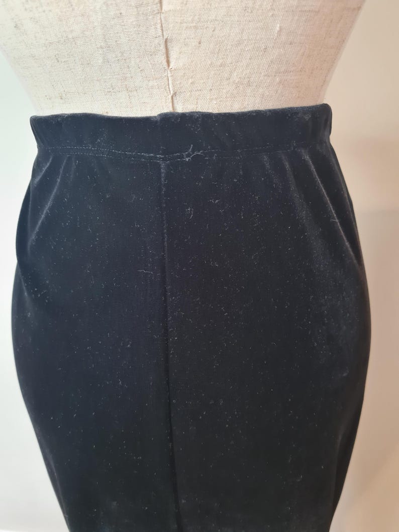 May include: A black velvet skirt with a straight silhouette. The skirt is made of a soft, smooth fabric and has a simple design.