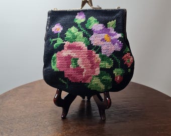 以下が含まれることがあります： 花柄の刺繍が施された黒い布製の財布。花はピンク、紫、緑。財布は金属製の留め具が付いている。