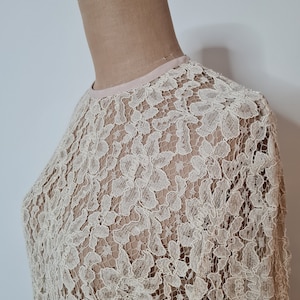 May include: A delicate off-white lace top with a round neckline. The lace has a floral pattern.