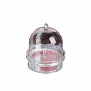 May include: A clear plastic dome cake stand with a round base and three legs. The stand is designed to display and protect cakes, pastries, or other desserts.