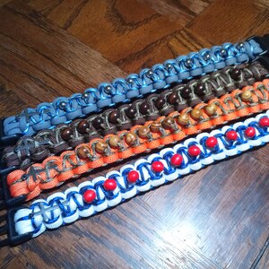 Pu&ograve; includere: Cinque braccialetti in paracord colorati con diverse perline e dettagli metallici. I braccialetti sono realizzati con una variet&agrave; di colori, tra cui blu, arancione, marrone e grigio. Ogni braccialetto ha una chiusura in metallo.