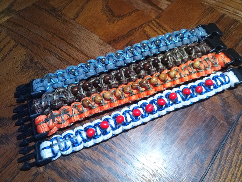 Pu&ograve; includere: Cinque braccialetti in paracord colorati con diverse perline e dettagli metallici. I braccialetti sono realizzati con una variet&agrave; di colori, tra cui blu, arancione, marrone e grigio. Ogni braccialetto ha una chiusura in metallo.