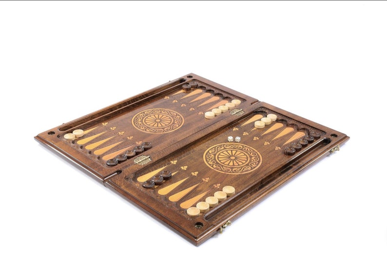 May include: A wooden backgammon set with intricate carvings and a traditional design. The board is open, revealing the playing surface and the pieces.