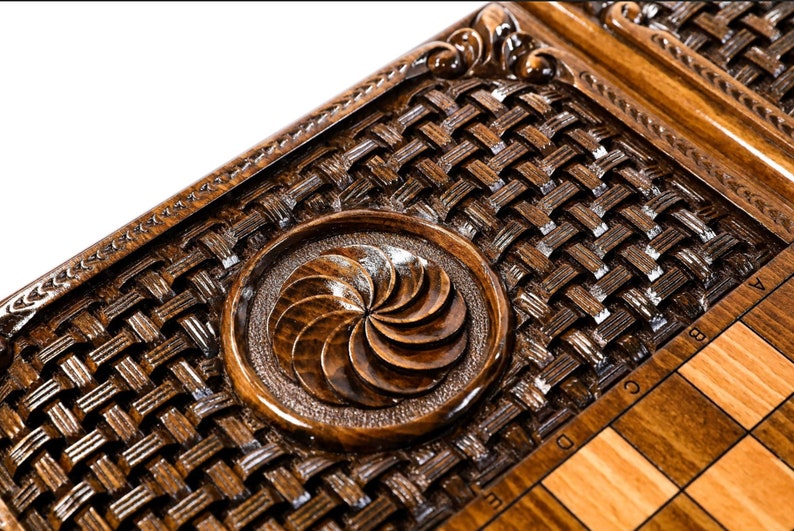 May include: A wooden chessboard with a decorative inlay of a woven pattern and a carved circular design. The chessboard is made of dark wood with light wood squares.
