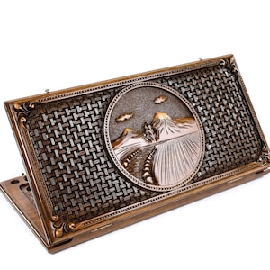 May include: A wooden game box with a carved design of a mountain landscape. The box has a woven pattern on the lid and is closed.