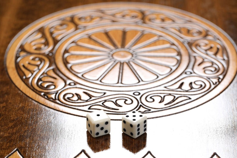 May include: Two white dice with black dots on a wooden game board with an intricate carved design. The dice are in the centre of the board.
