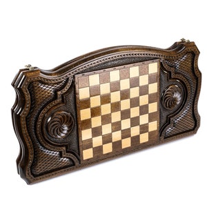 Puede incluir: Un tablero de ajedrez de madera con intrincados tallados en el exterior. El tablero est&aacute; cerrado y las piezas de ajedrez no son visibles.