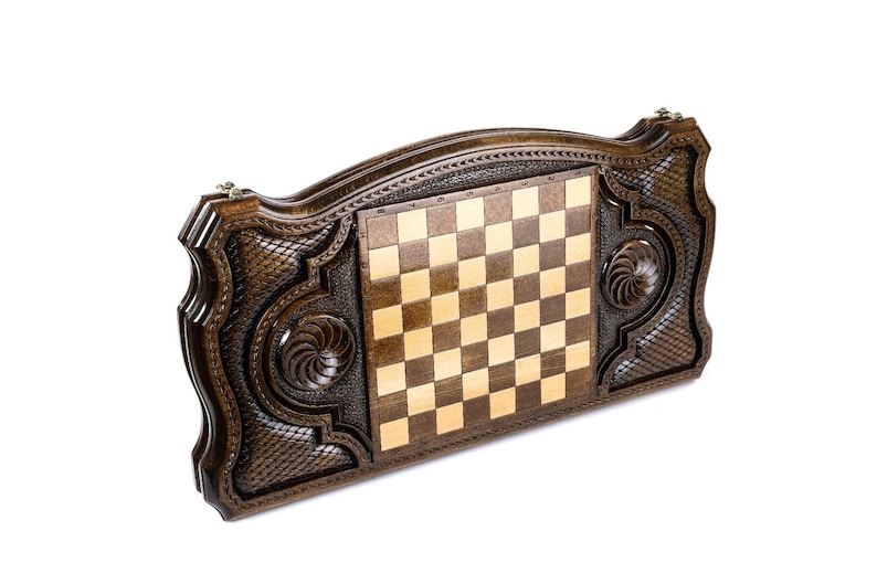 Puede incluir: Un tablero de ajedrez de madera con intrincados tallados en el exterior. El tablero est&aacute; cerrado y las piezas de ajedrez no son visibles.