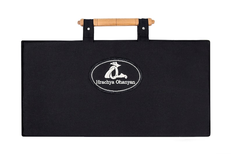 Puede incluir: Estuche de transporte de lona negra con asa de madera y un logotipo ovalado bordado en blanco que dice "Hrachya Ohanyan".