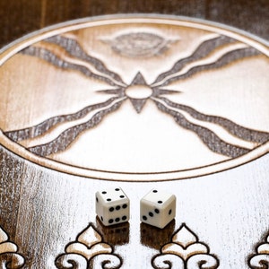 Puede incluir: Dos dados blancos con puntos negros en un tablero de juego de madera con un dise&ntilde;o tallado en el centro.