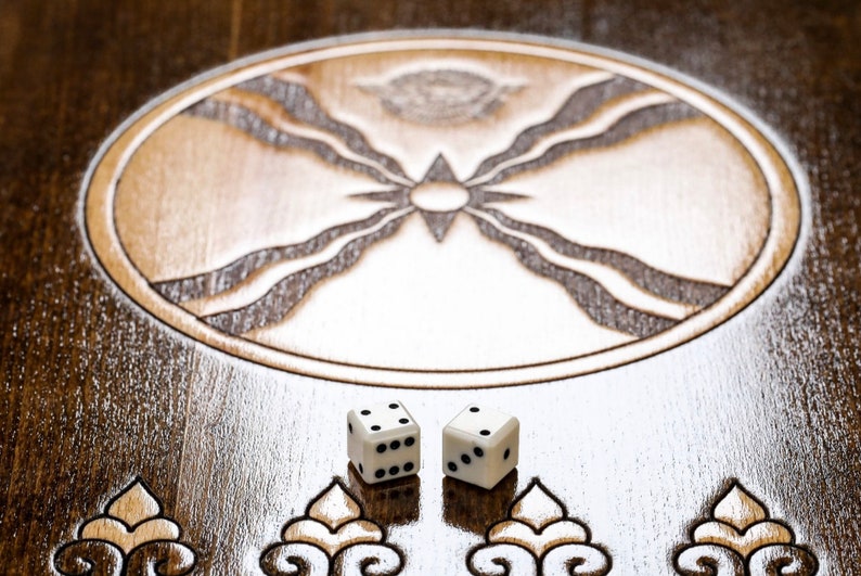 Puede incluir: Dos dados blancos con puntos negros en un tablero de juego de madera con un dise&ntilde;o tallado en el centro.