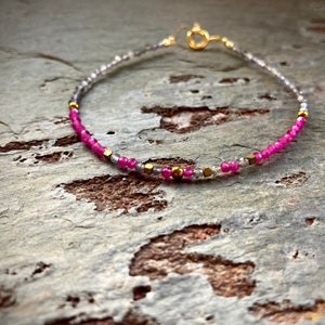 May include: A delicate bracelet with pink and clear beads, interspersed with gold accents. The bracelet is made with small, round beads and has a simple, elegant design.